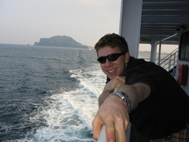 Henry on a ferry, with the wake and coastline behind him.