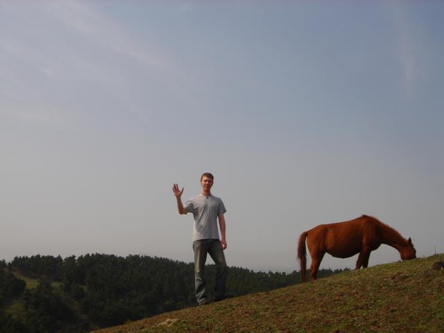 A traveler beside a grazing horse on a grassy hillside.